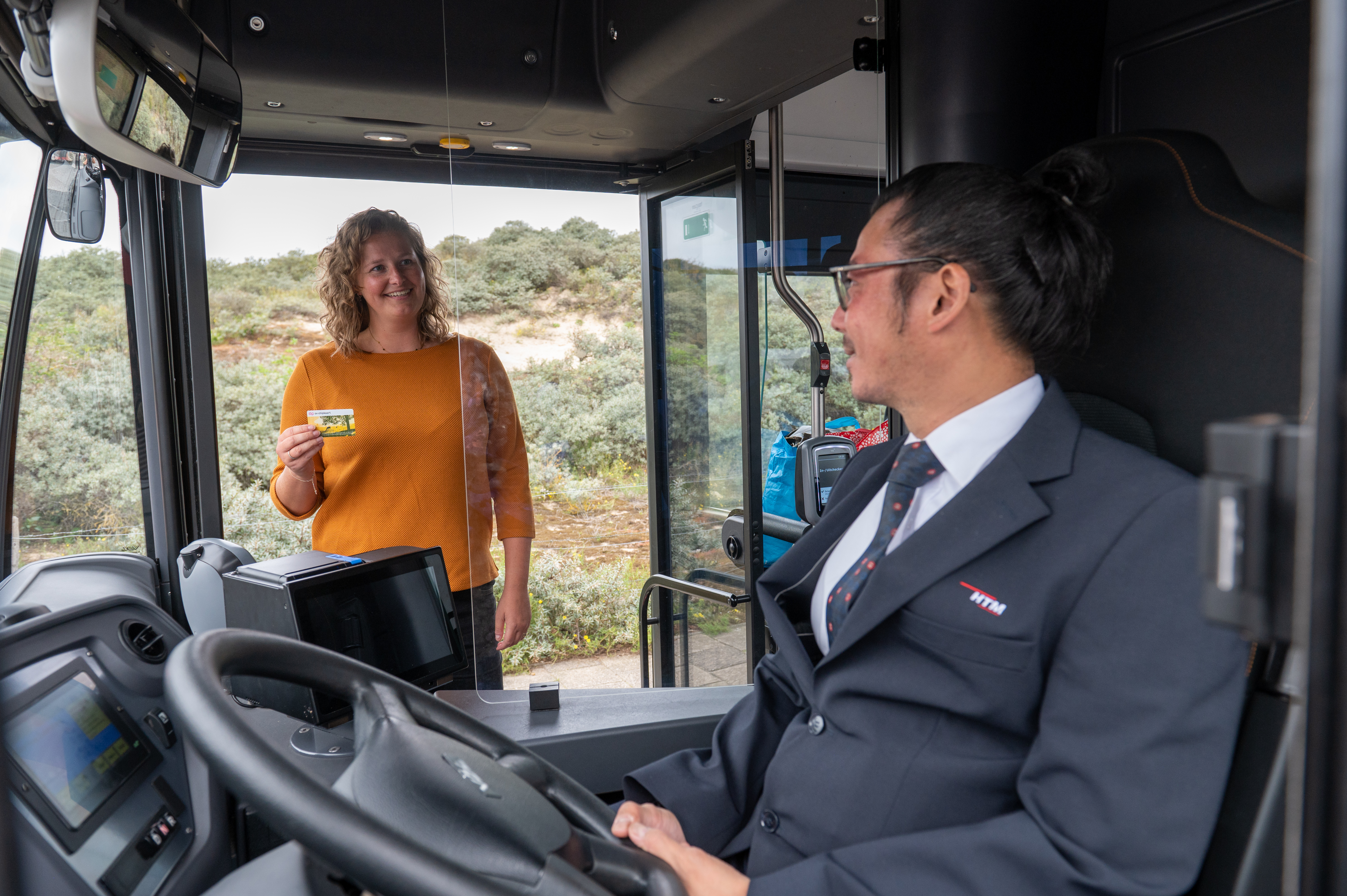 Buschauffeur zit achter het stuur van HTM bus en groet reiziger